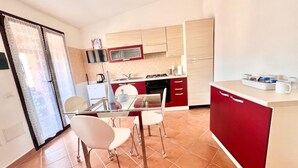 A modern kitchen with a dining area, featuring a glass table, red and white cabinetry, and a tiled floor. - Hadley House Key to Villas (Viddalba)
