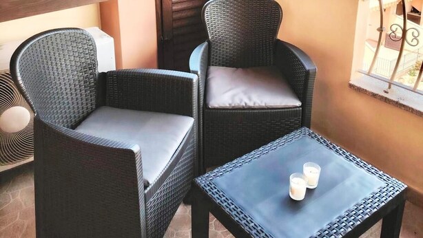 A balcony with wicker furniture, a small table, and a view of buildings in the background. - Hadley House Key to Villas (Viddalba)