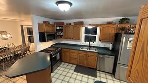 Una cocina con armarios de madera, una estufa negra, un lavamanos de acero inoxidable y un refrigerador.