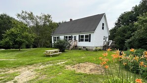 Una casa con techo inclinado, un porche delantero y un pequeño jardín con flores.