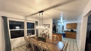 Un comedor con una mesa y sillas de madera, un lámpara colgante y vistas a la cocina.