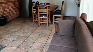 A living room with a brick wall, a dining table with chairs, a refrigerator, and a sofa. - La Casa de los Abuelos (Santiago Tepetlapa)