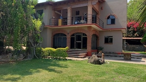 A two-story house with a balcony, a front door, and a small garden area. - La Casa de los Abuelos (Santiago Tepetlapa)