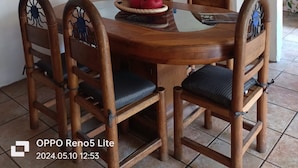 A dining area with a round wooden table, four chairs with intricate back designs, a red abstract painting, a tiled ceiling, and a brick archway leading to another room. - La Casa de los Abuelos (Santiago Tepetlapa)