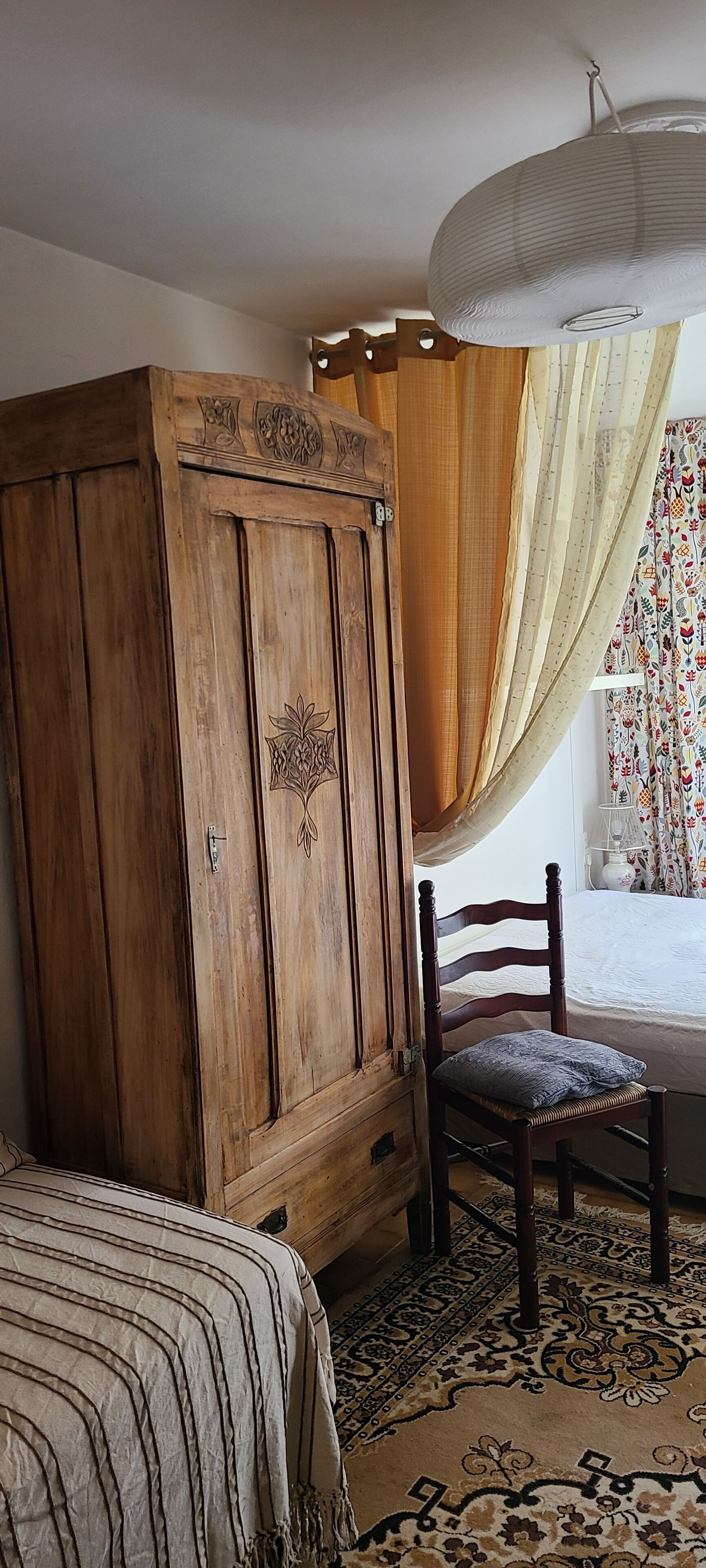 Un dormitorio con un armario de madera, una silla, una cama con cubrecama a rayas y una alfombra estampada.