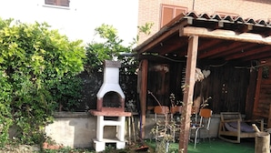 A rustic outdoor area with a brick oven, wooden chairs, and a small garden with an agave plant. - B&B Ma Maison Govone  (Govone)
