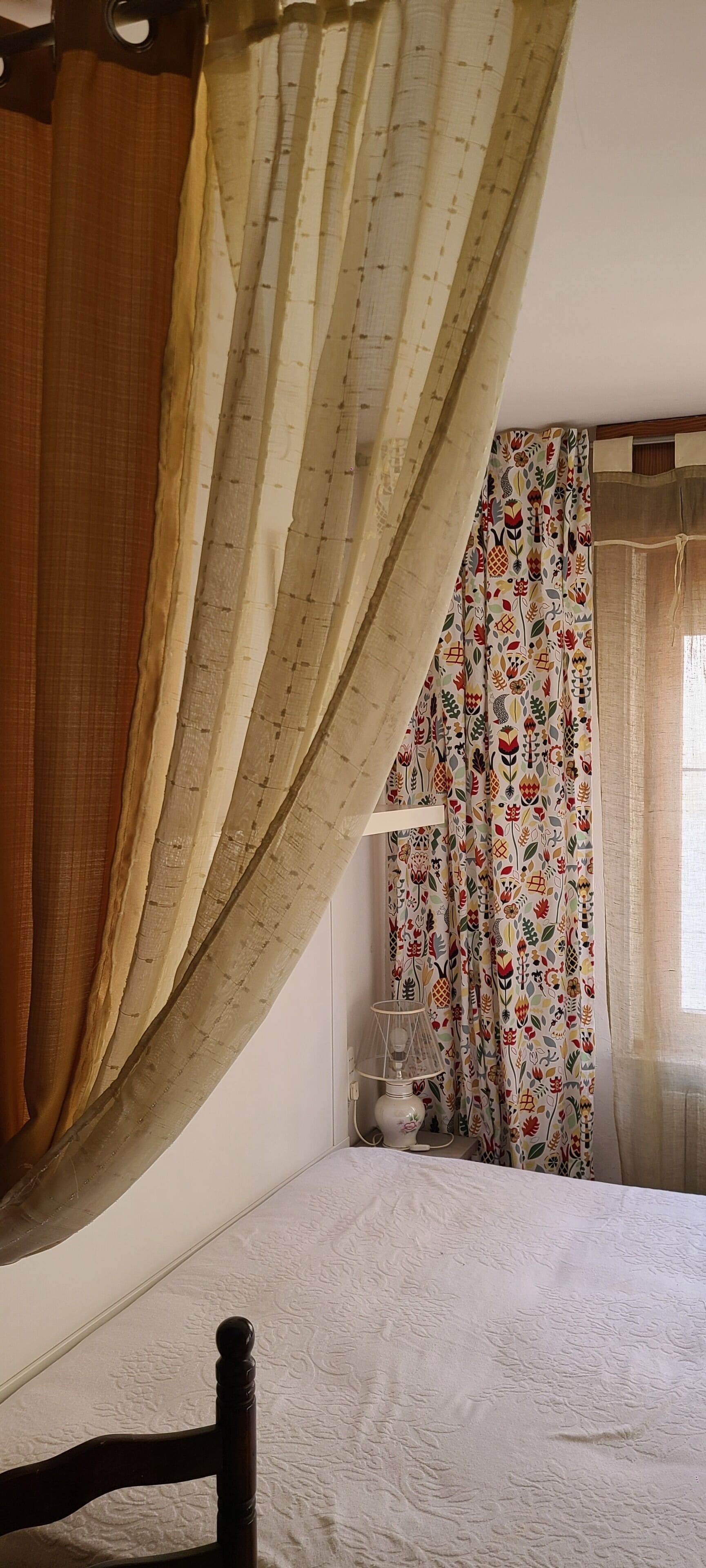 A bedroom with a bed, curtains, and a bedside table with a lamp.