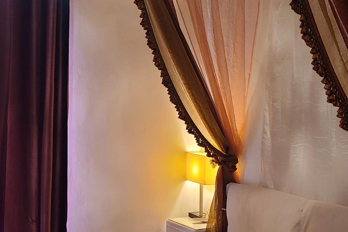 Un lit à baldaquin, une table de chevet avec une lampe et un appareil de climatisation fixé au mur.