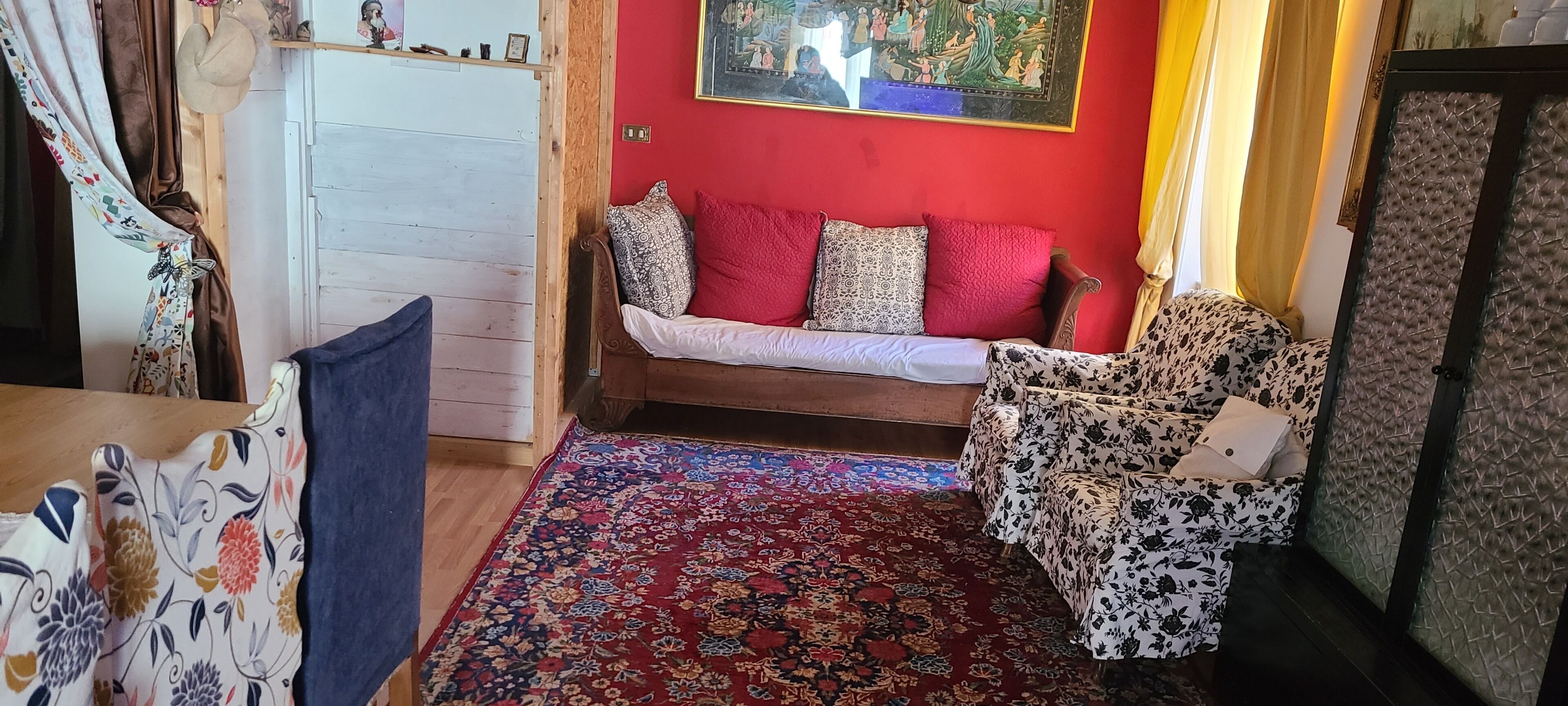 A cozy room with a wooden floor, a red wall, a patterned sofa, and a floral rug.