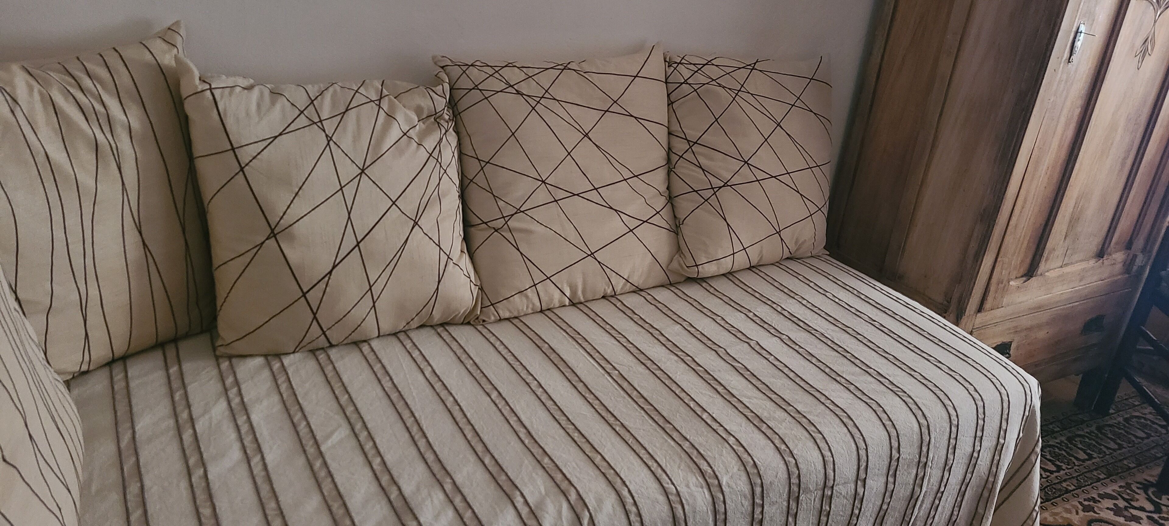 Un canapé beige recouvert d’un tissu à rayures, agrémenté de coussins aux motifs géométriques.