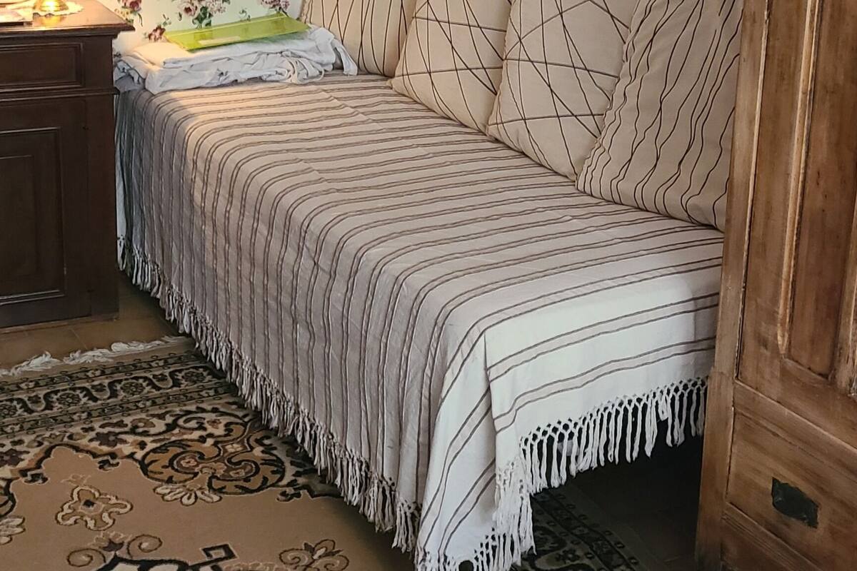Une chambre à coucher avec un lit, une table de chevet, une lampe, un papier peint à motifs floraux, un tapis à motifs et une porte en bois.