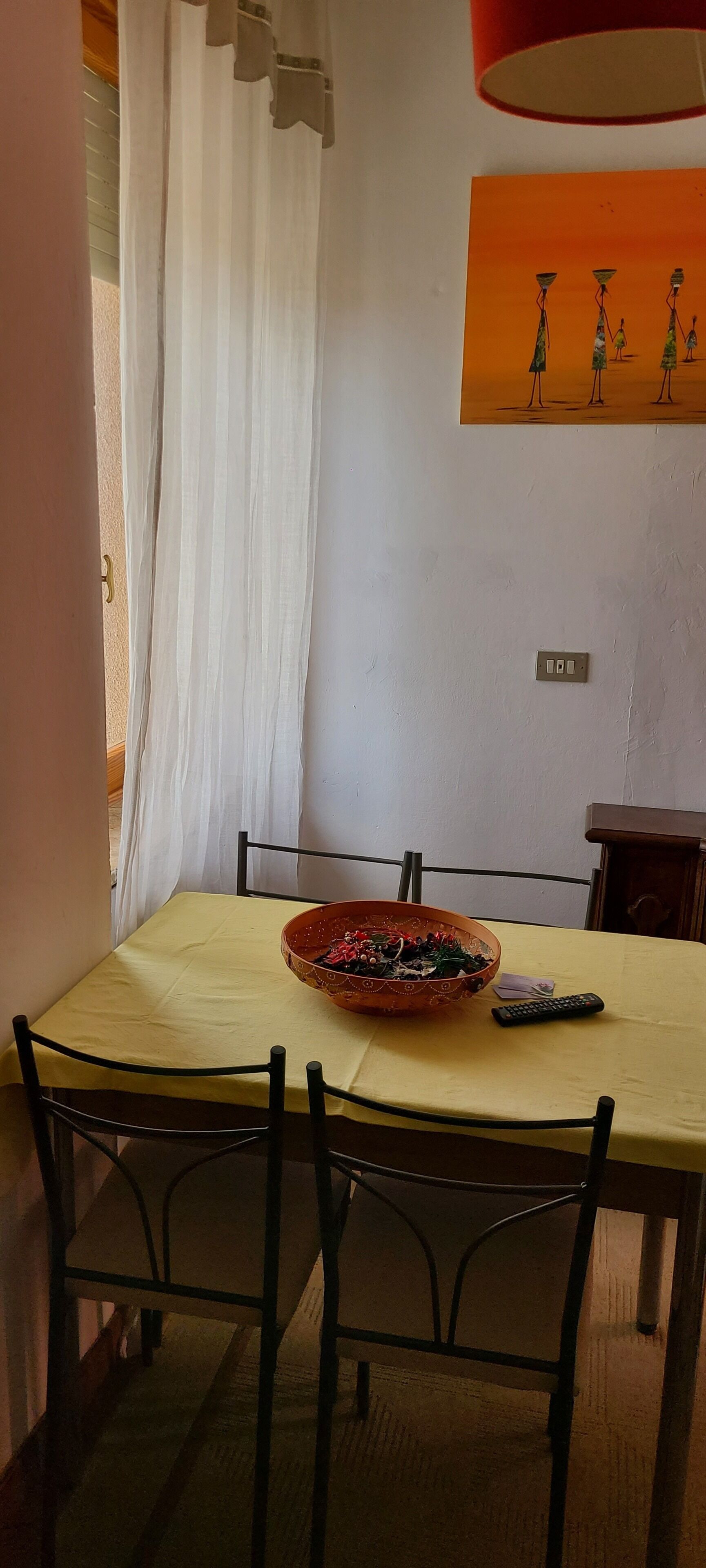 A dining area with a table set for two, featuring a decorative bowl and a remote control.