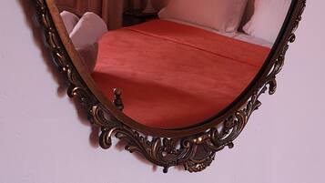 Une chambre à coucher avec un grand miroir décoratif, un lit recouvert d’une couverture rouge et un tableau encadré représentant un papillon accroché au mur.