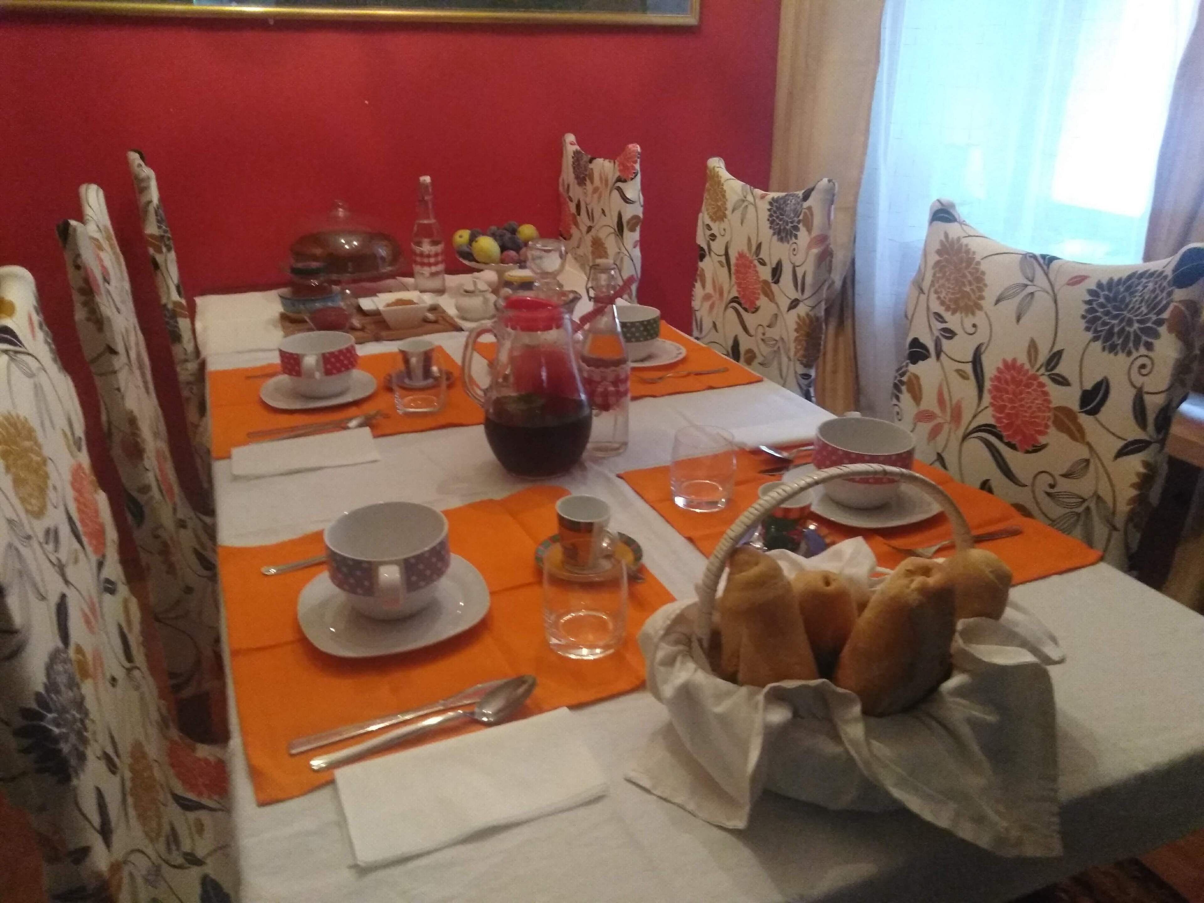 Una mesa de comedor con manteles individuales anaranjados, mantel blanco y sillas estampadas con motivos florales.
