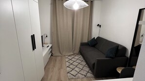 A modern, compact living space with a kitchenette, a sofa, a patterned rug, and a pendant light.