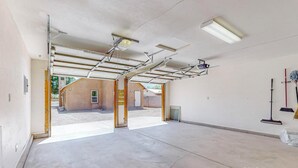 A spacious indoor area with a concrete floor, metal ceiling beams, and a partially open garage door leading outside.