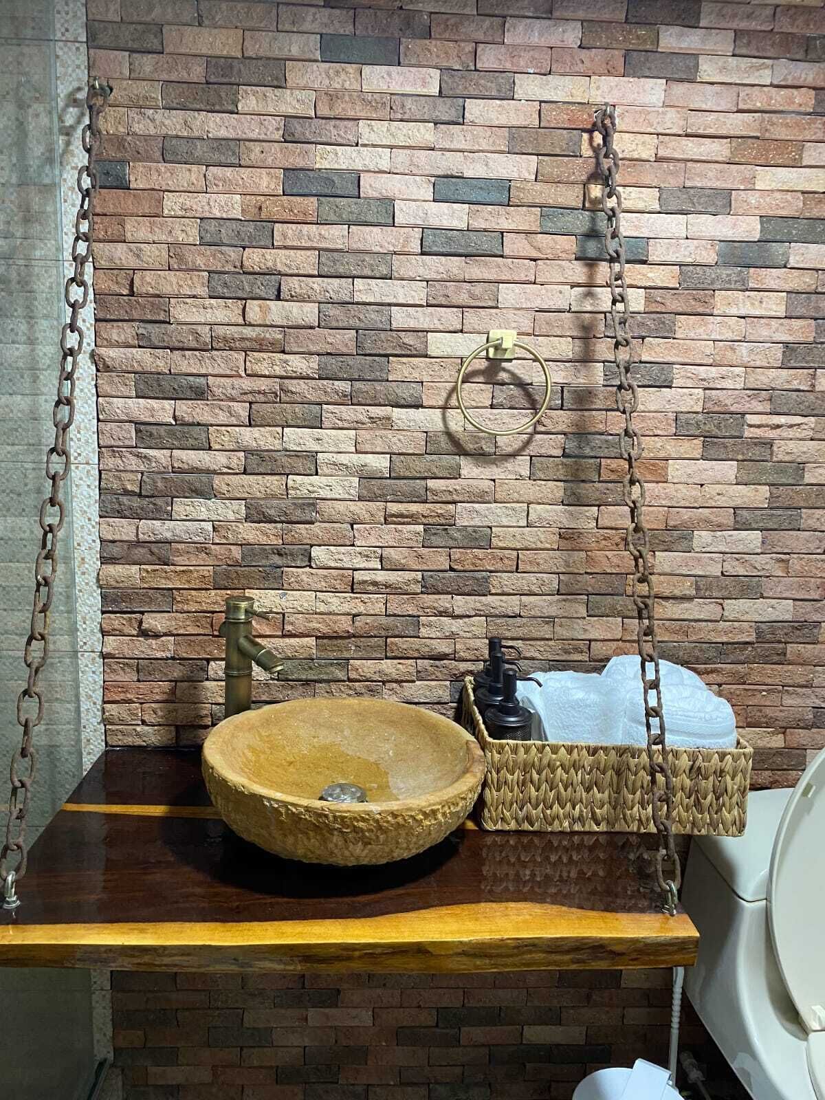 A rustic bathroom with a stone sink, a wooden shelf, and a brick wall.