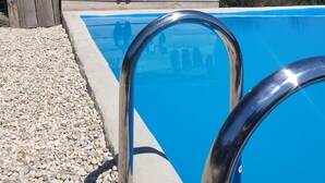 Una piscina con cubierta de madera y guijarros, rodeada por un cerramiento de madera con plantas en macetas.