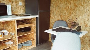 Cocina compacta con microondas integrado, refrigerador y comedor con una silla gris y una mesita.