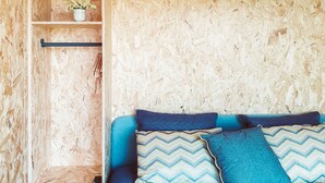 Una habitación con una cama, un estante con una planta y una pared hecha de virutas de madera.