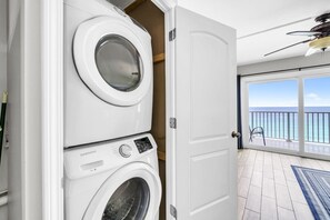 Une buanderie équipée d’une machine à laver et d’un sèche-linge superposés, et une porte donnant sur un balcon avec vue sur l’océan.