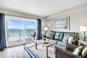 A living room with a green leather sofa, a coffee table, a side table with a lamp, and a view of the beach through a sliding glass door. - BeachFront-Summit 629 (Panama City Beach)