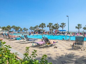 A poolside area with lounge chairs, a swimming pool, and palm trees.