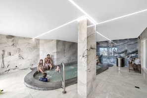 A modern indoor pool area with marble walls and a central pool, surrounded by seating and a trash bin. - BeachFront-Summit 629 (Panama City Beach)