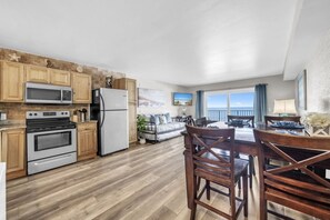 A kitchen with wooden cabinets, a refrigerator, an oven, and a microwave. There is a dining area with a table and chairs. - BeachFront-Summit 629 (Panama City Beach)