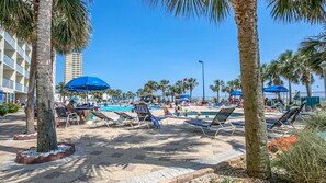A poolside area with lounge chairs and umbrellas, surrounded by palm trees and a clear blue sky. - BeachFront-Summit 507 (Panama City Beach)