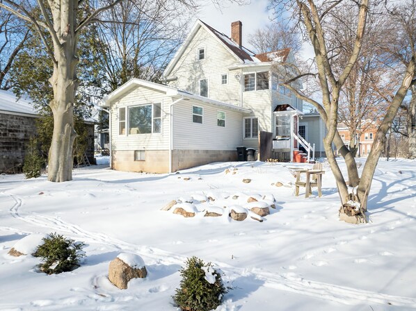 A two-story house with a large front porch, a chimney, and a snow-covered yard.