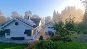 Duas casas de madeira branca com painéis solares, um deck de madeira e um jardim com uma árvore.