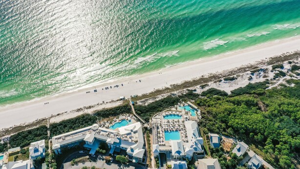 An aerial view of a coastal resort with multiple swimming pools, beach access, and lush greenery.