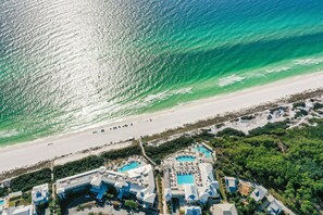 An aerial view of a coastal resort with multiple swimming pools, beach access, and lush greenery.