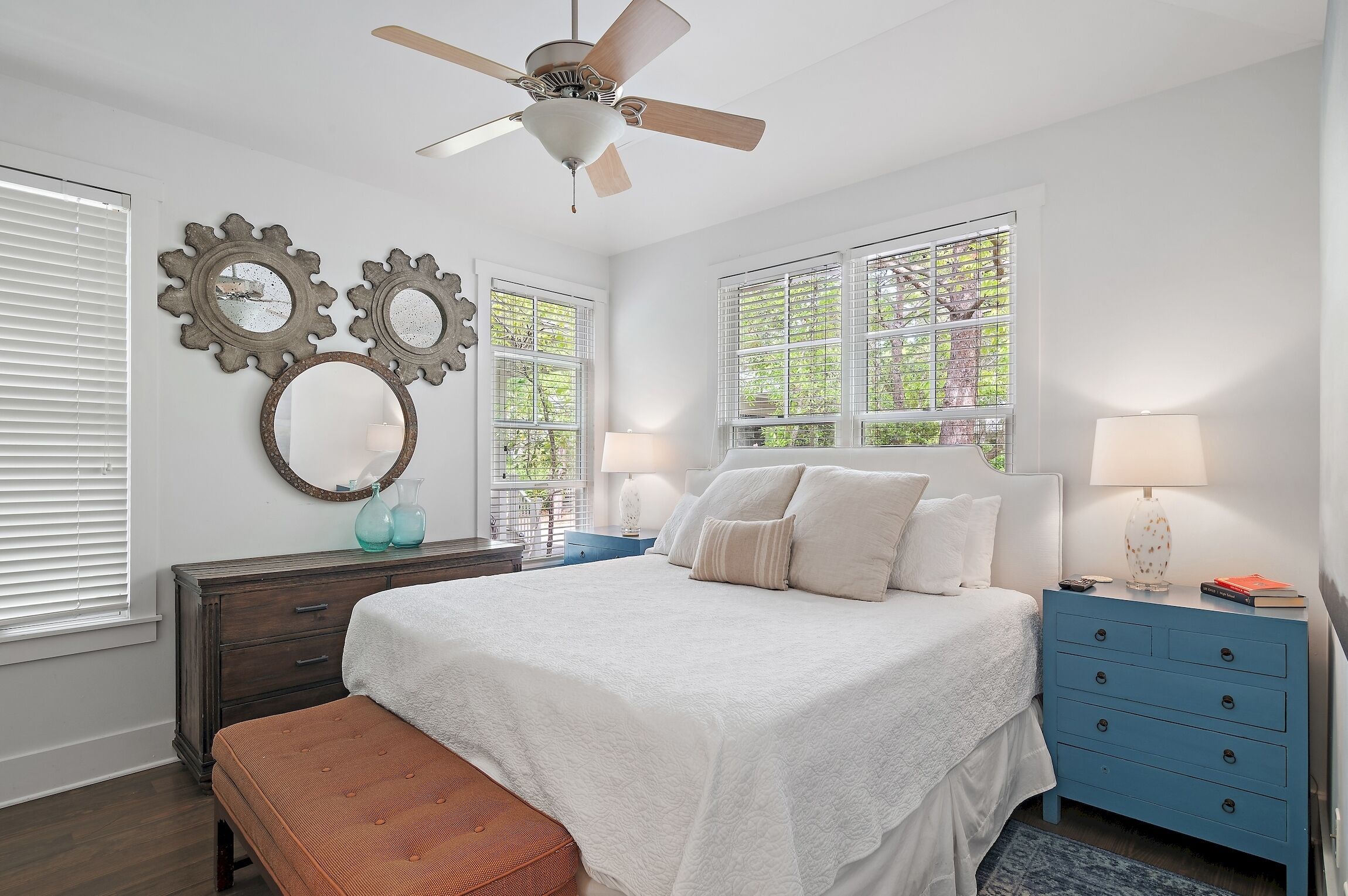 A bedroom with a bed, a nightstand, a dresser, a ceiling fan, and decorative wall mirrors.