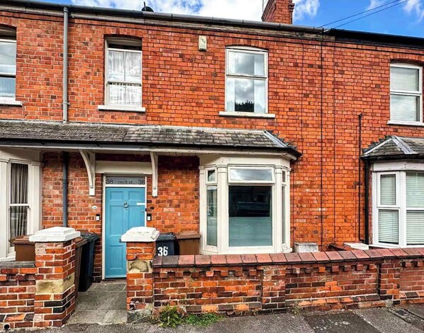 A red brick terraced house with a blue door, a bay window, and a number '36' on the wall.