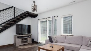 Ein modernes Wohnzimmer mit Treppe, Flachbildfernseher, grauem Sofa und Couchtisch.