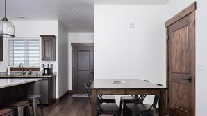 Eine moderne Küche mit dunklem Holzboden, einer zentralen Kochinsel mit Barhocker und einem Esstisch mit Stühlen.