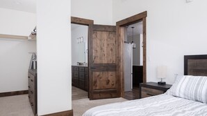 Ein Schlafzimmer mit Bett, Schminktisch, Nachttisch und Holztür zu einem anderen Raum.