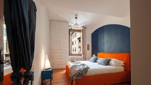 A bedroom with an orange bed, white and blue pillows, a small bedside table, and a ceiling fan. - Cate Apartment - Flo Apartments (Firenze)