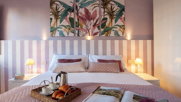 A neatly made bed with striped bedding, a bedside table with a lamp, and a wall art piece above.