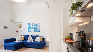 A modern living room with a blue sectional sofa, a small side table with a lamp, and a painting on the wall.
