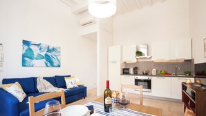 A modern living room with a blue sofa, dining table with plates and wine glasses, and a kitchen in the background.