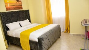 A bed with a grey headboard, white bedding, and a yellow accent. - Stylish fully furnished 2 bedroom  2 bath in Kitale 5 min from city center  (Kitale)