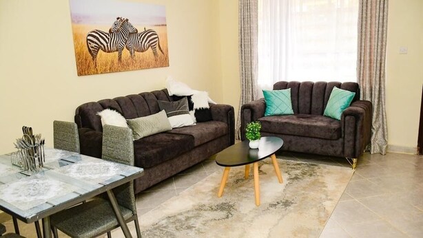 A living room with two sofas, a glass coffee table, and a dining table with chairs. - Stylish fully furnished 2 bedroom  2 bath in Kitale 5 min from city center  (Kitale)