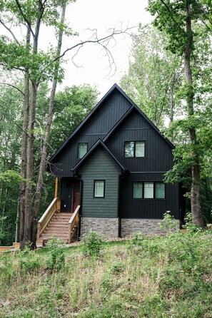 Een modern huis met twee verdiepingen, een steil dak, een houten trap naar de voordeur en een stenen fundering.
