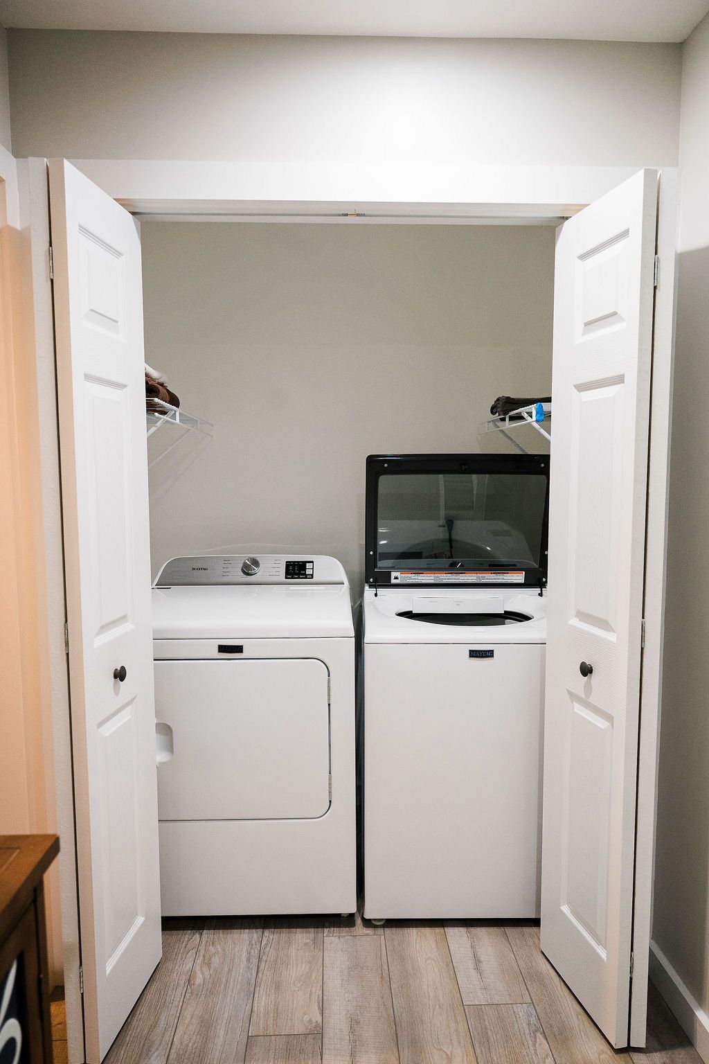 A laundry room with two white front-loading washers and dryers, wooden flooring, and white walls.