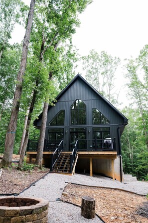 A modern cabin with a large glass front, wooden deck, and a stone fire pit. - Gorgeous new 3 bdr house right by entrance to Dale Hollow Lake State Resort Park (Burkesville)