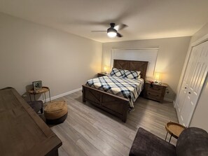 A bedroom with a bed, bedside tables, a ceiling fan, a window with blinds, and a wardrobe.