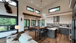 Eine moderne Küche mit Steinrückwand, ein Essbereich mit großem Fenster und eine Wohnarea mit weißem Sofa.